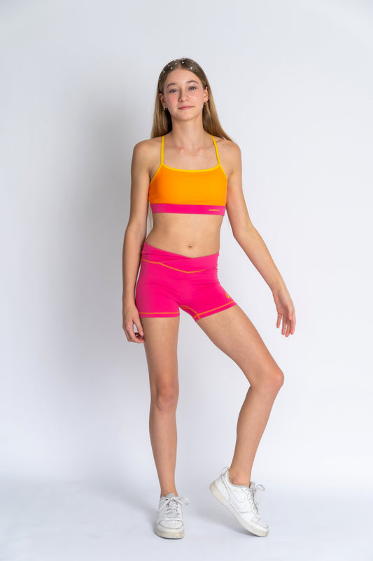 A female model wearing a crop top and shorts in vibrant summer colors, standing against a plain background.