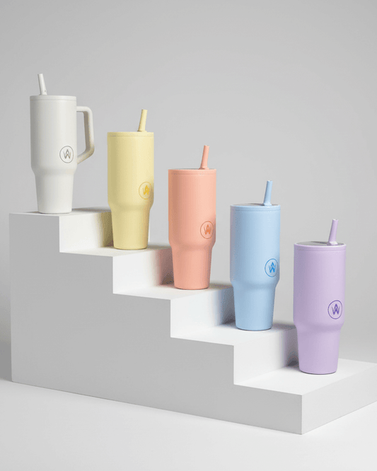 Set of colorful tumblers with straws on a geometric shelf against a gray background