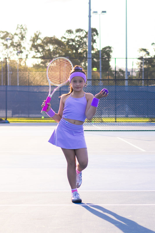 Young girl in purple tennis outfit holding a racket on a tennis court.