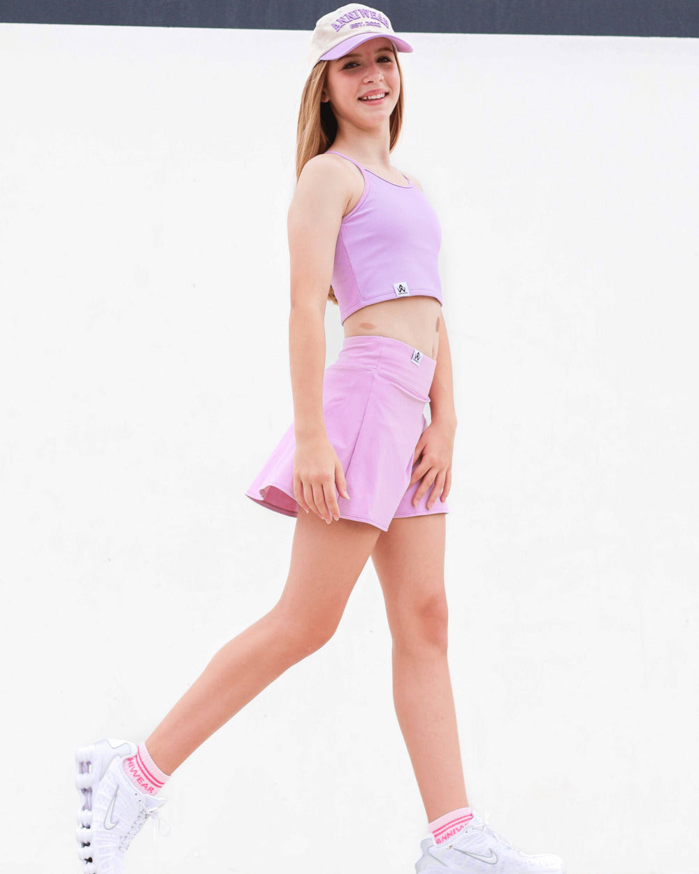 Young girl in pink lavender athletic outfit with matching cap on a white background