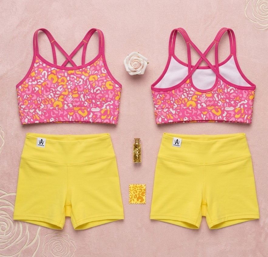 Two pink sports bras with floral patterns and yellow shorts on a pink background.
