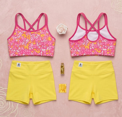 Two pink sports bras with floral patterns and yellow shorts on a pink background.