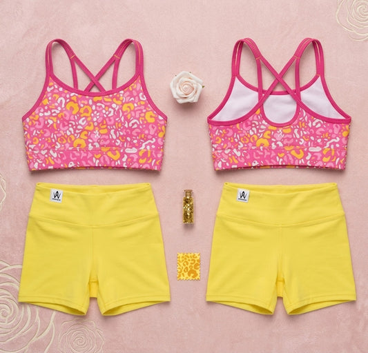 Two pink sports bras with floral patterns and yellow shorts on a pink background.