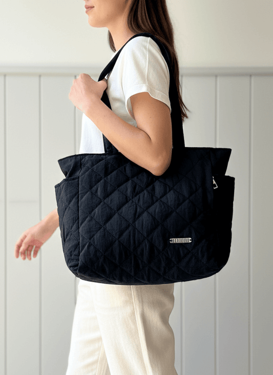 Person holding a black quilted tote bag against a white background