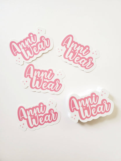 Die cut waterproof vinyl stickers with the text 'Anni Wear' in pink color, surrounded by small pink dots.