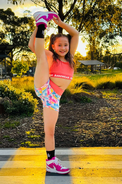 Young girl in colorful athletic wear performing a high leg stretch outdoors.