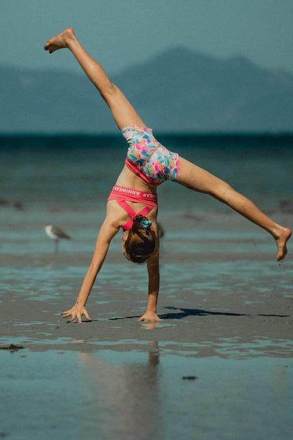 Young girl performing a handstand on a beach with mountains in the background