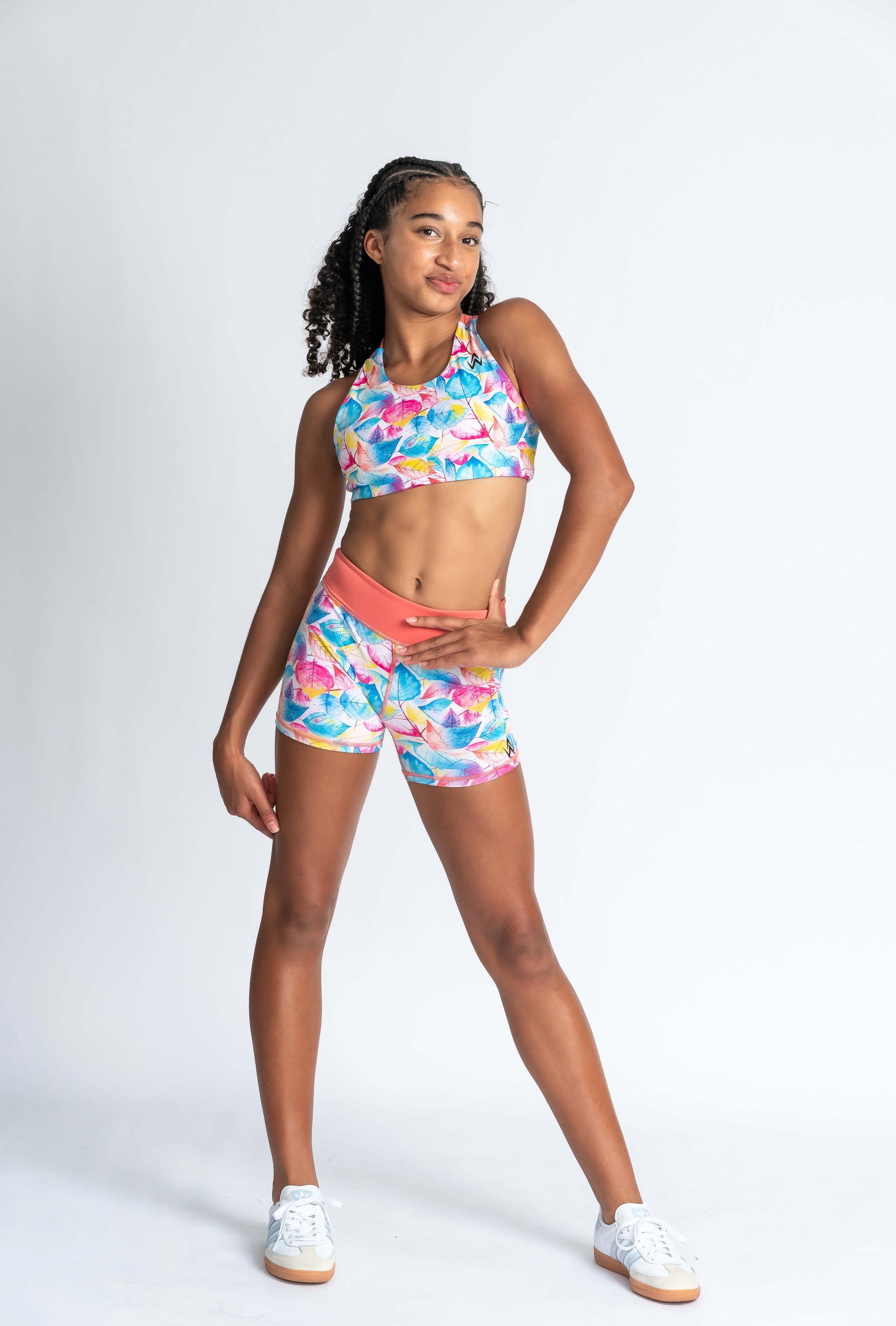 A female model wearing a multicolored floral crop top and matching shorts, standing against a white background.