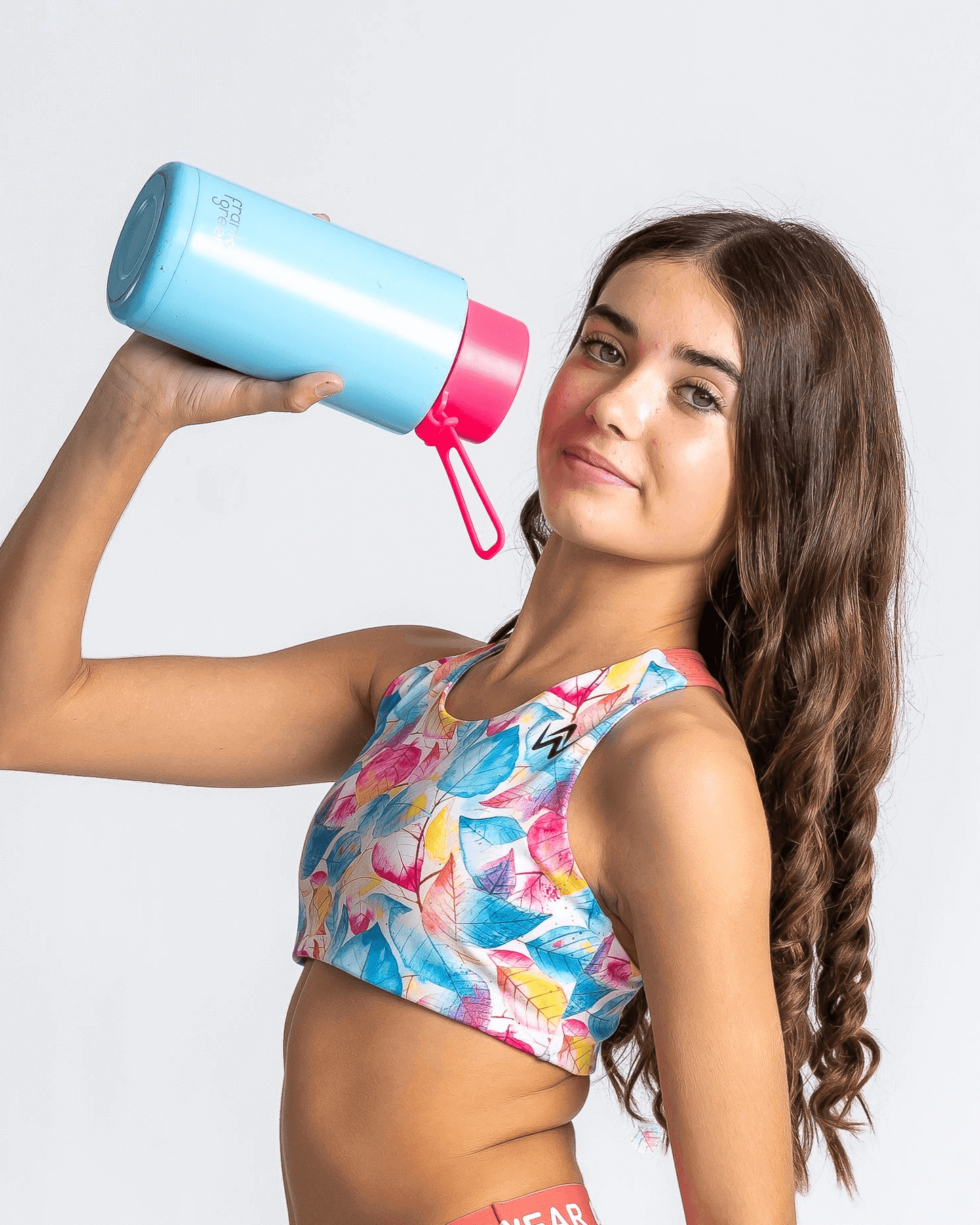 Girl wearing a tropical coloured crop holding a blue and pink water bottle against a white background