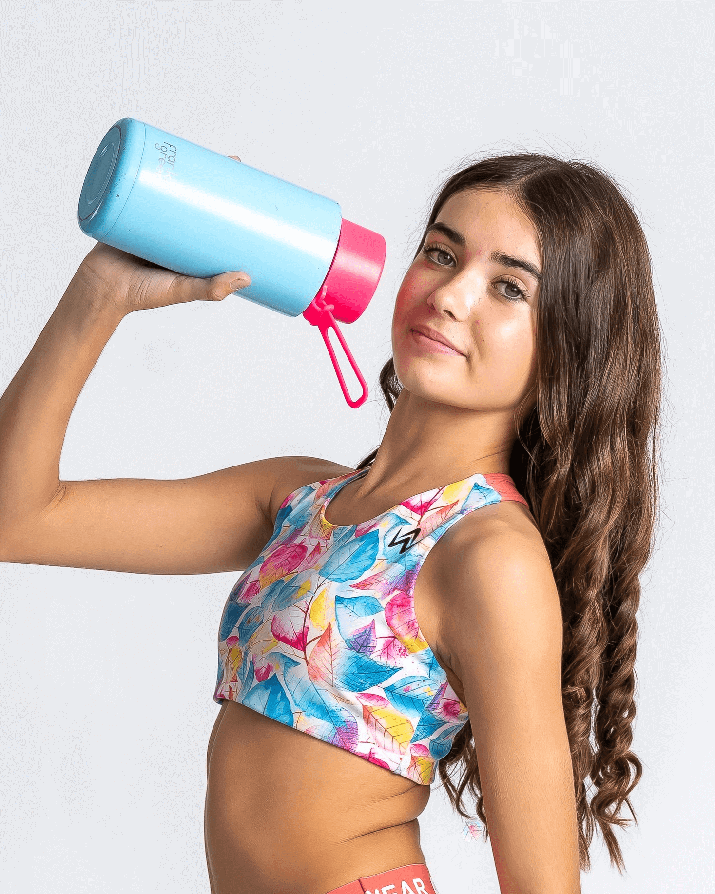 Girl wearing a tropical coloured crop holding a blue and pink water bottle against a white background
