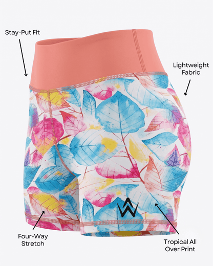 A pair of women's athletic shorts with a coral pink waistband and a tropical leaf print in blue, pink, yellow, and white. The image includes text callouts and arrows pointing to features like 'Stay-Put Fit,' 'Lightweight Fabric,' 'Four-Way Stretch,' and 'Tropical All Over Print.