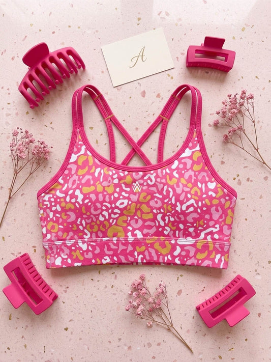 Pink sports crop top with animal print surrounded by pink hair accessories on a light background