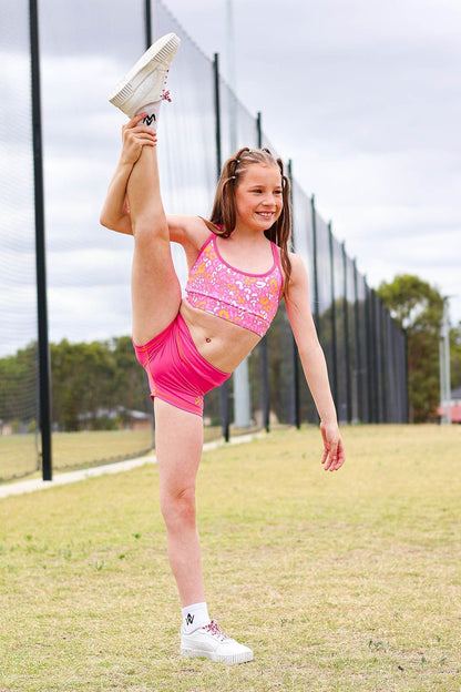 Young girl in a pink sportswear outfit stretching outdoors.