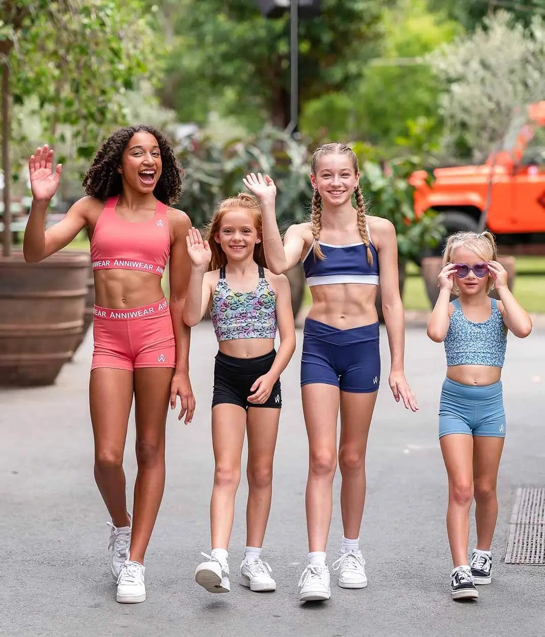 Four girls that are teens and tweens wearing colorful Anniwear activewear sets smiling and waving hands